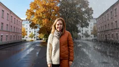 Nainen seisoo kadulla, taustalla syksyinen ja sateinen maisema, syksymuoti.