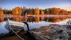 Mies veneen vieressä järven rannalla, syksyiset värit ja heijastukset vedessä.