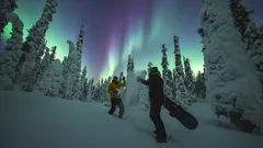 Revontulet Lapissa, luminen metsä, kaksi lumilautailijaa talviyössä.