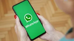 Nainen pitää puhelinta, jossa näkyy WhatsApp-sovelluksen aloitusnäyttö