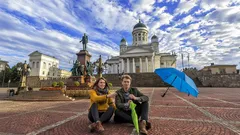 Kaksi ihmistä Helsingin Senaatintorilla, taustalla tuomiokirkko ja sininen sateenvarjo.