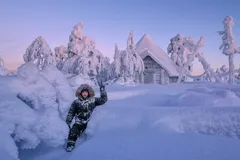 Henkilö seisoo lumisessa Lapin maisemassa mökin edessä, ympärillä talviset puut.